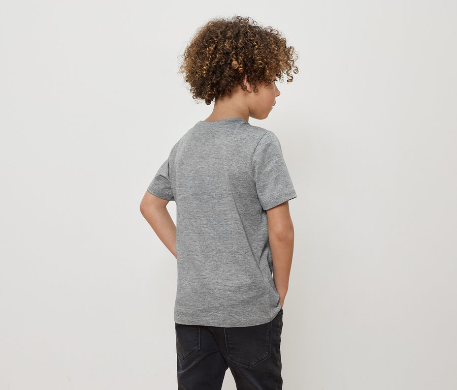 Chlapec s kudrnatými vlasy stojí zády k fotoaparátu a má na sobě šedé tričko a černé džíny.