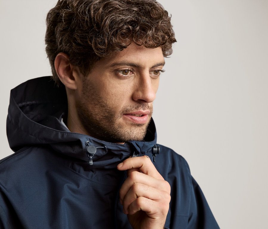 Muž s kudrnatými vlasy v tmavě modré bundě s kapucí.