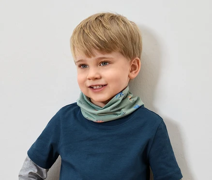 Usmívající se chlapec s blond vlasy v modrém tričku má na sobě zelený šátek se zvířecím vzorem.