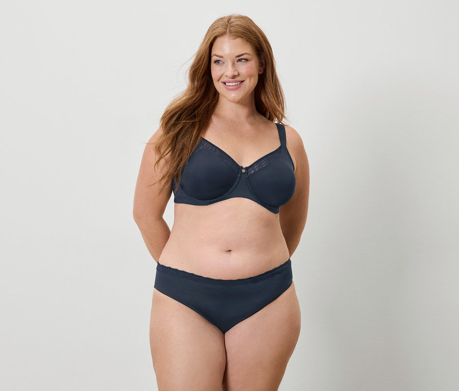 Žena s dlouhými rusými vlasy má na sobě tmavě modrou podprsenku a kalhotky a usmívá se.