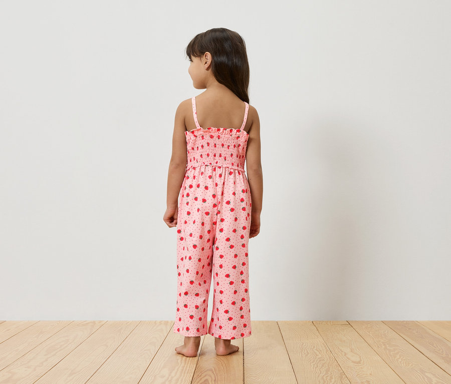 Dívka stojí zády ke kameře a má na sobě růžový overal s jahodovým vzorem.