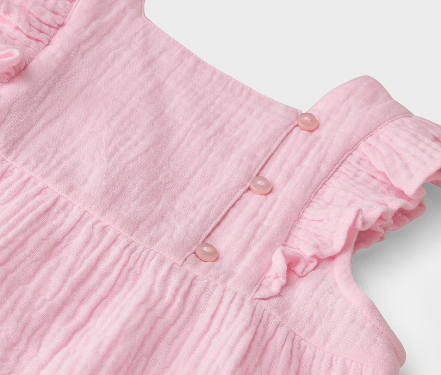 Detailní záběr na růžové šaty s volánky a knoflíky.