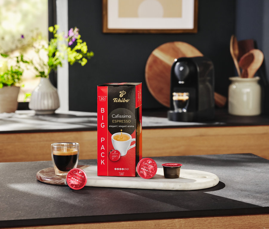 Na stole stojí balení kapslí Cafissimo Espresso, sklenice s espressem a kávovar.