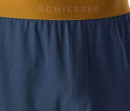 Modré pyžamové kalhoty s hnědo-zlatým pasem, na kterém je logo „SCHIESSER“.