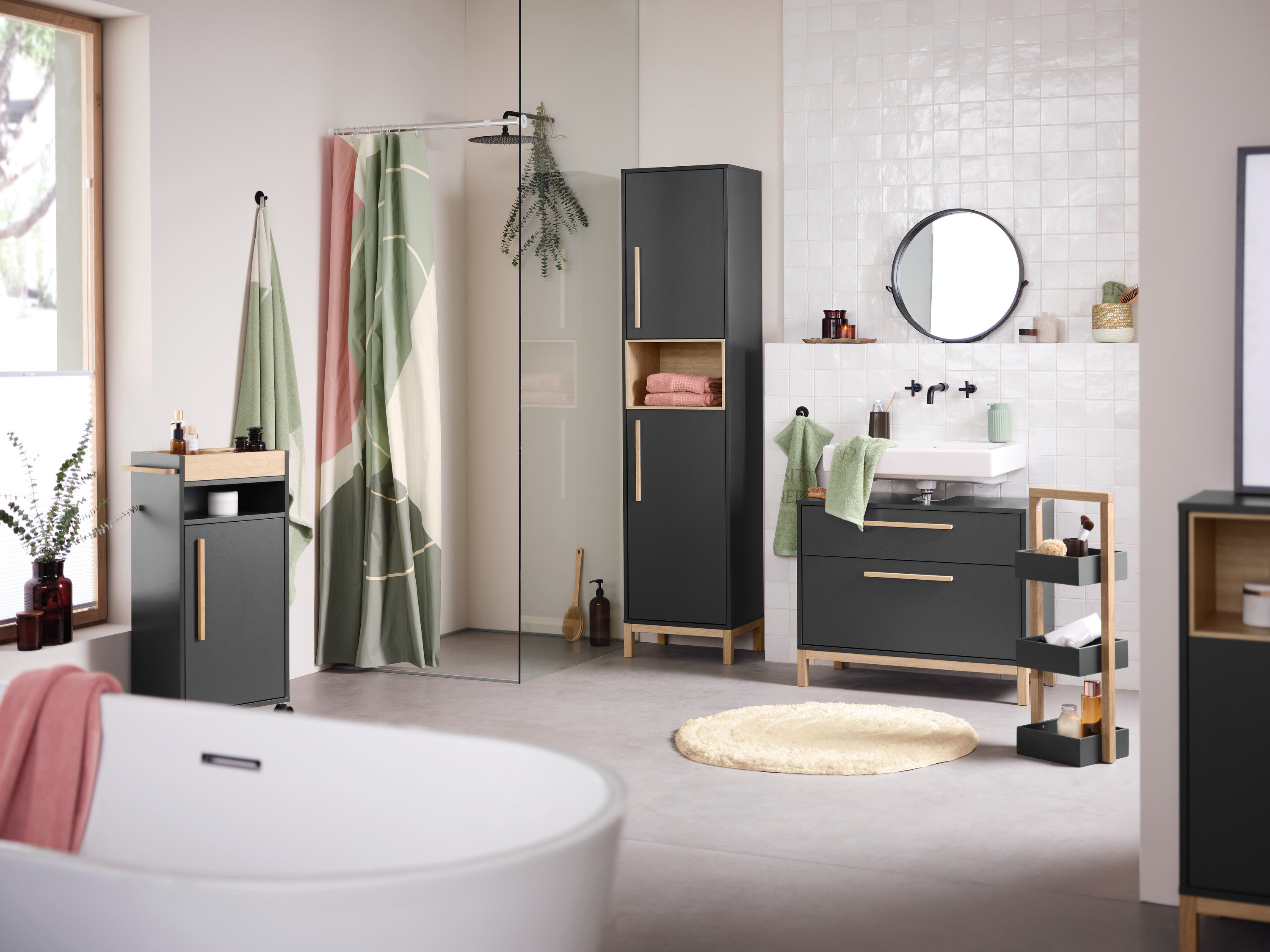 Interiér koupelny s umyvadlem, zrcadlem a úložnými skříňkami Eklund v antracitové barvě. V popředí je vana.
