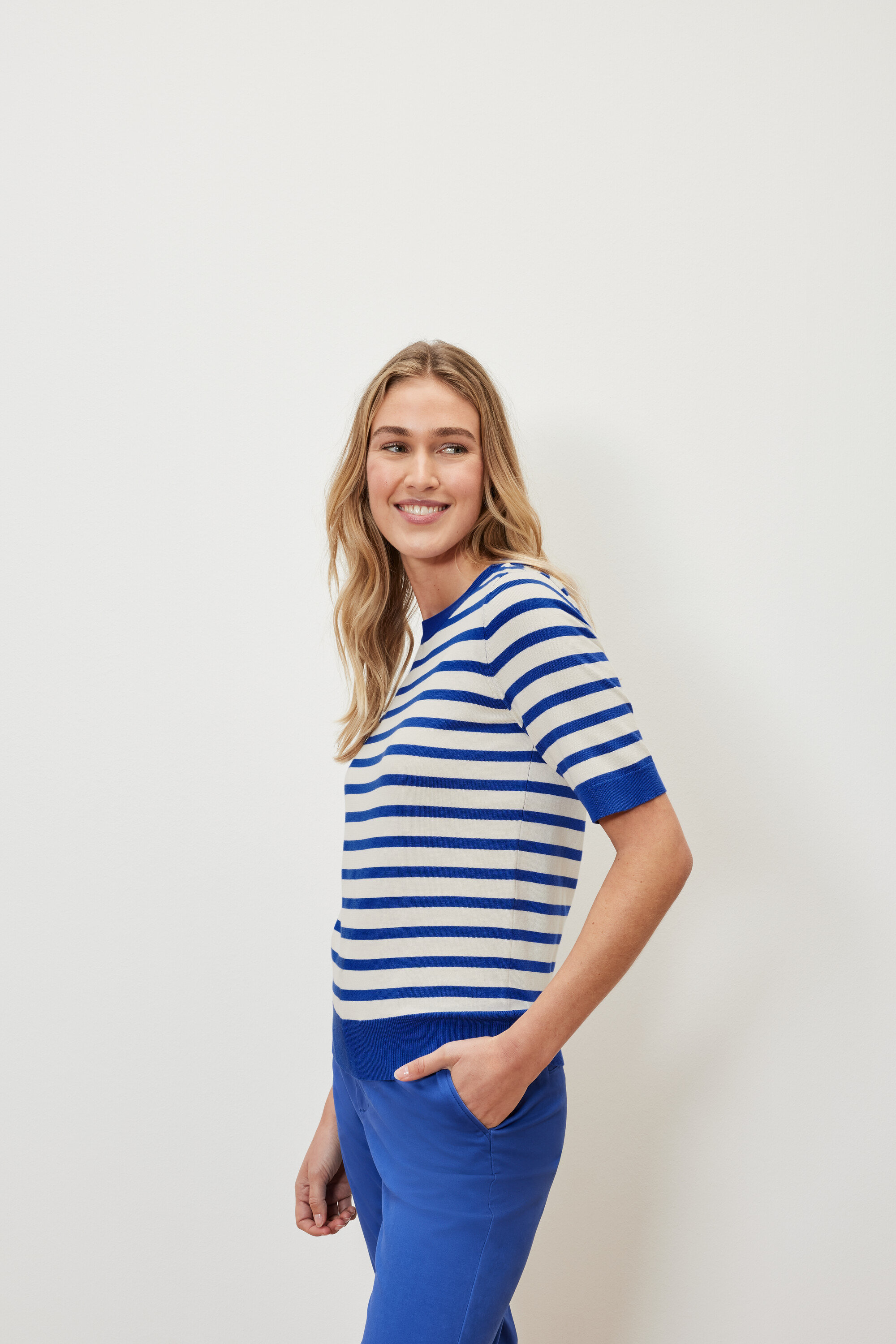 Žena má na sobě proužkovaný svetr z jemného úpletu a modré kalhoty.