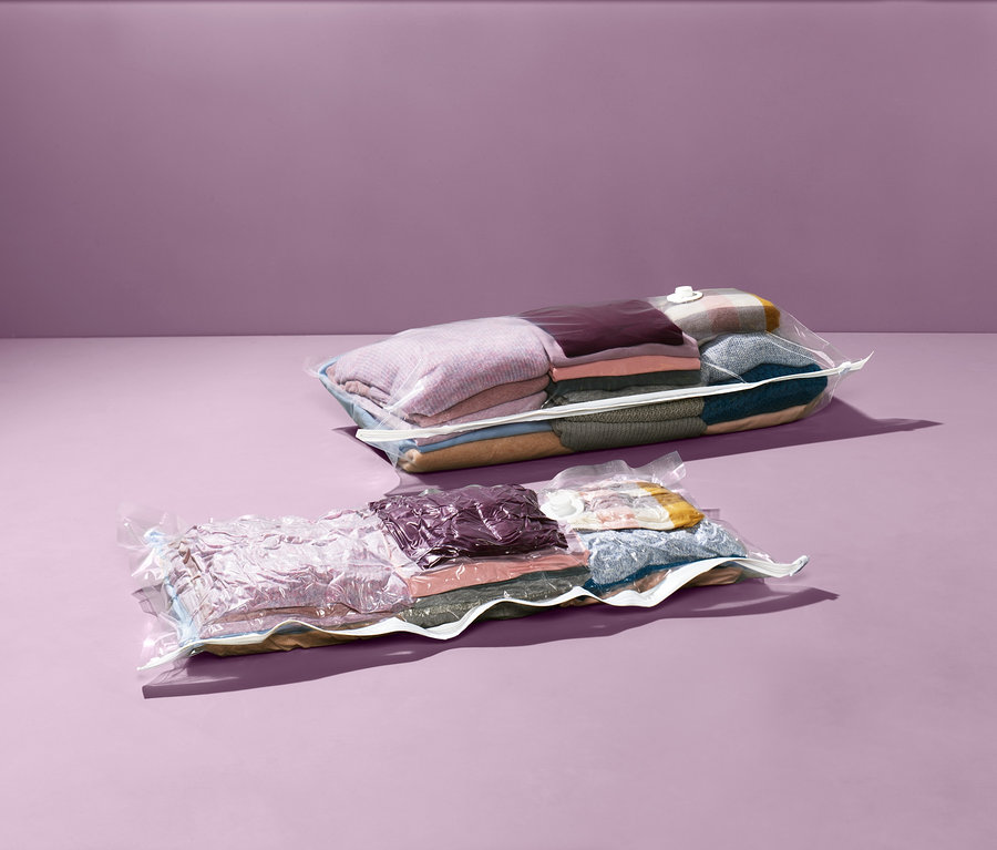 Dva vakuové úložné pytle s oblečením na fialovém pozadí.