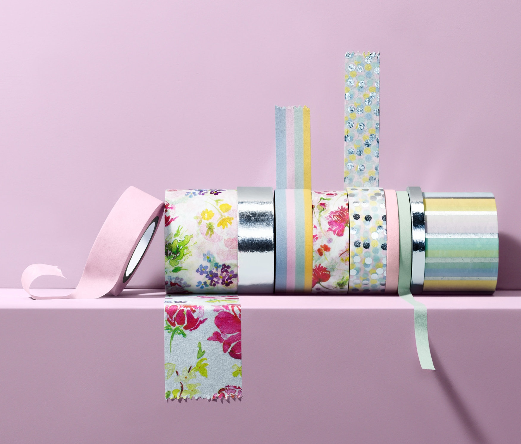 Na světle fialovém pozadí leží na světle fialové polici 10 dekoračních lepicích pásek.