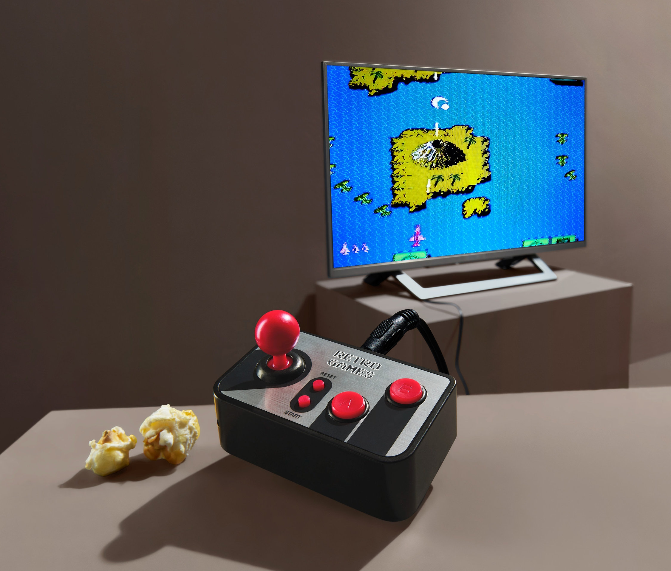 Retro herní TV konzole s joystickem a popcornem. V pozadí televize zobrazuje hru.