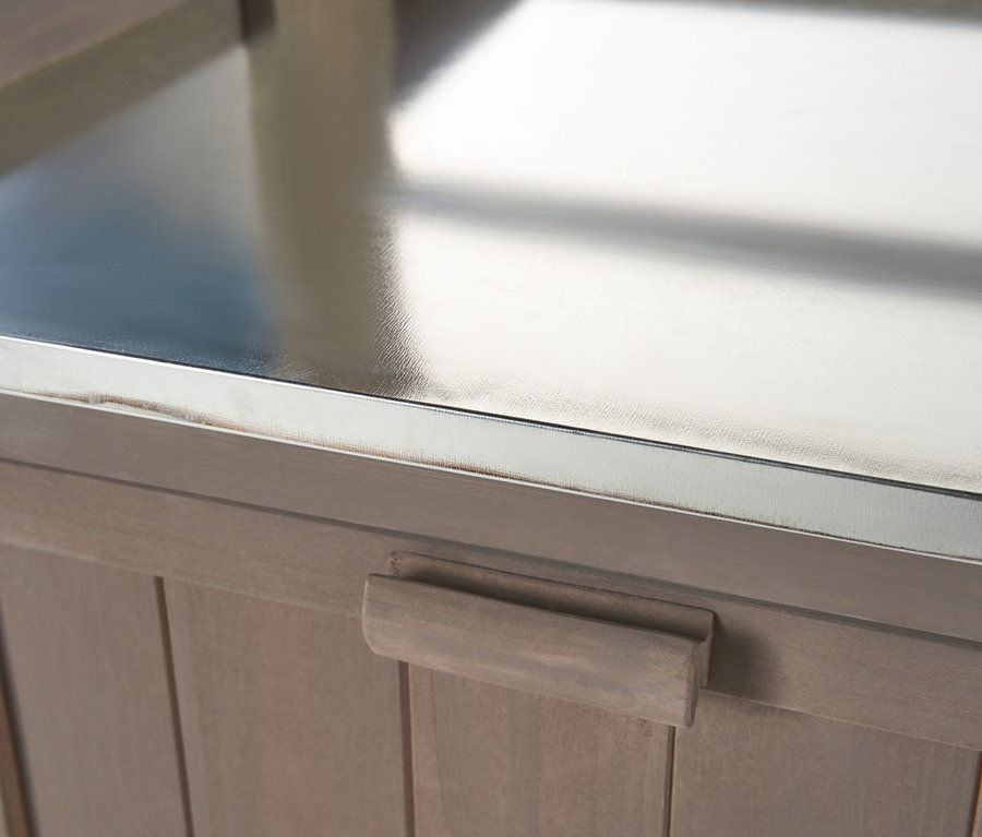 Detail zahradního stolku s regálem JONTE se stříbrnou pracovní deskou a dřevěnými dvířky.