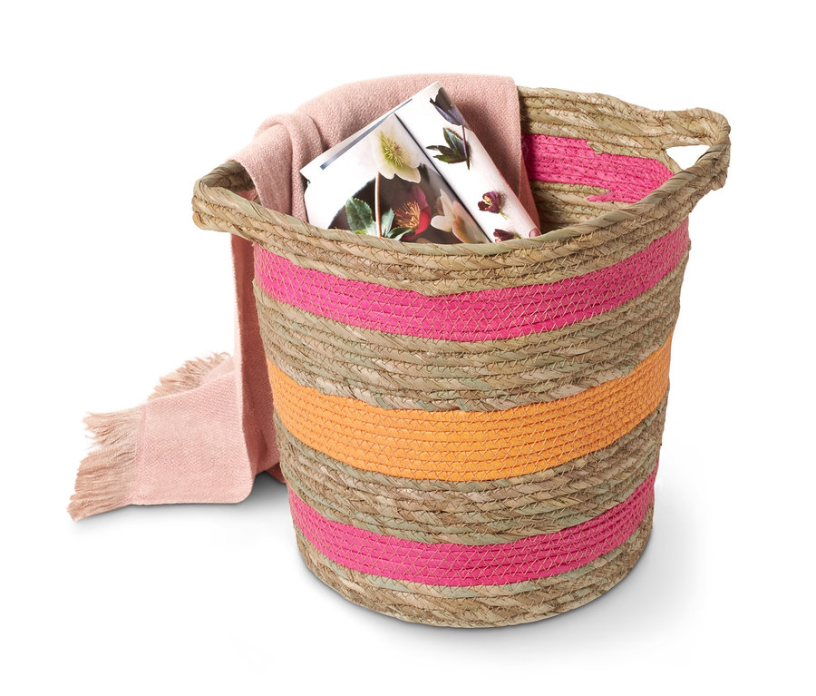 Proutěný dekorační košík s růžovými a oranžovými pruhy, uvnitř je růžová deka a časopis.