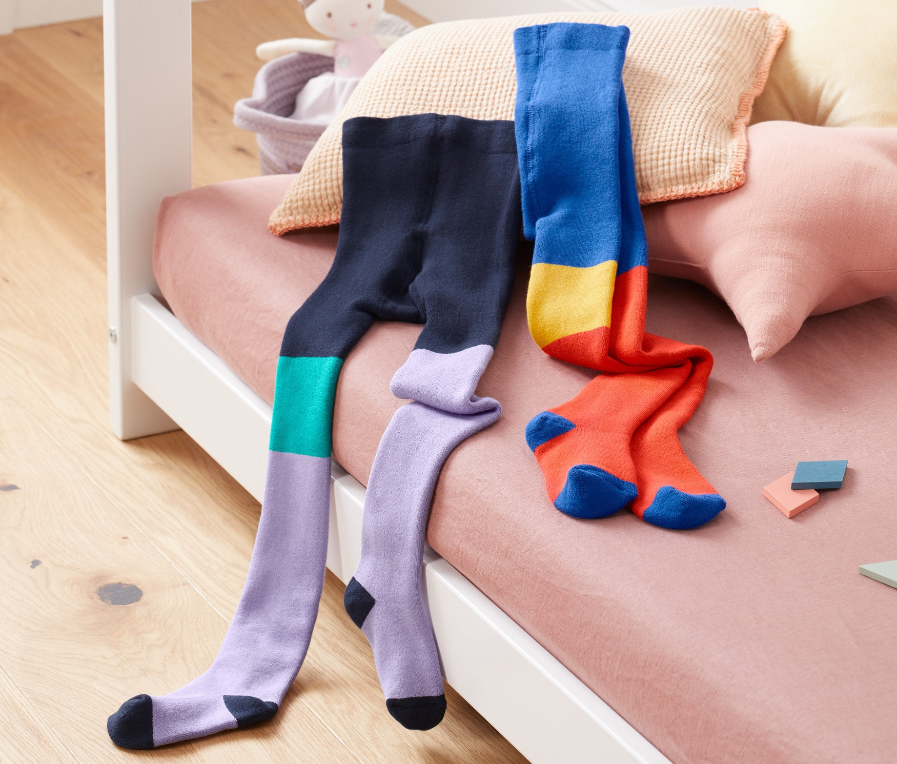 Dvoje termopunčocháče leží na posteli vedle sebe. Jedny jsou fialové, modré a zelené a druhé modré, žluté a červené.