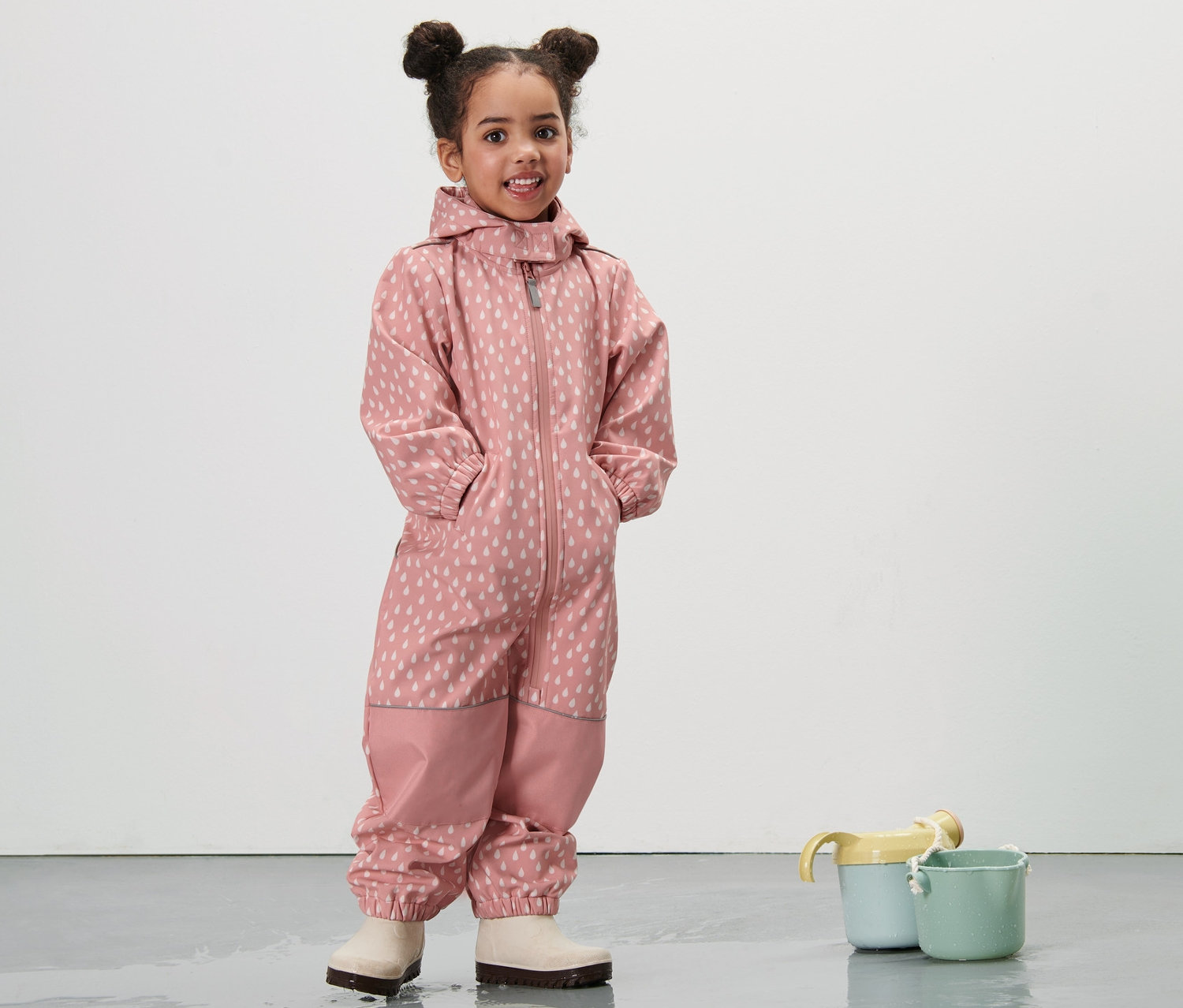 Dívka stojí v dětském softshellovém overalu s růžovými kapičkami.