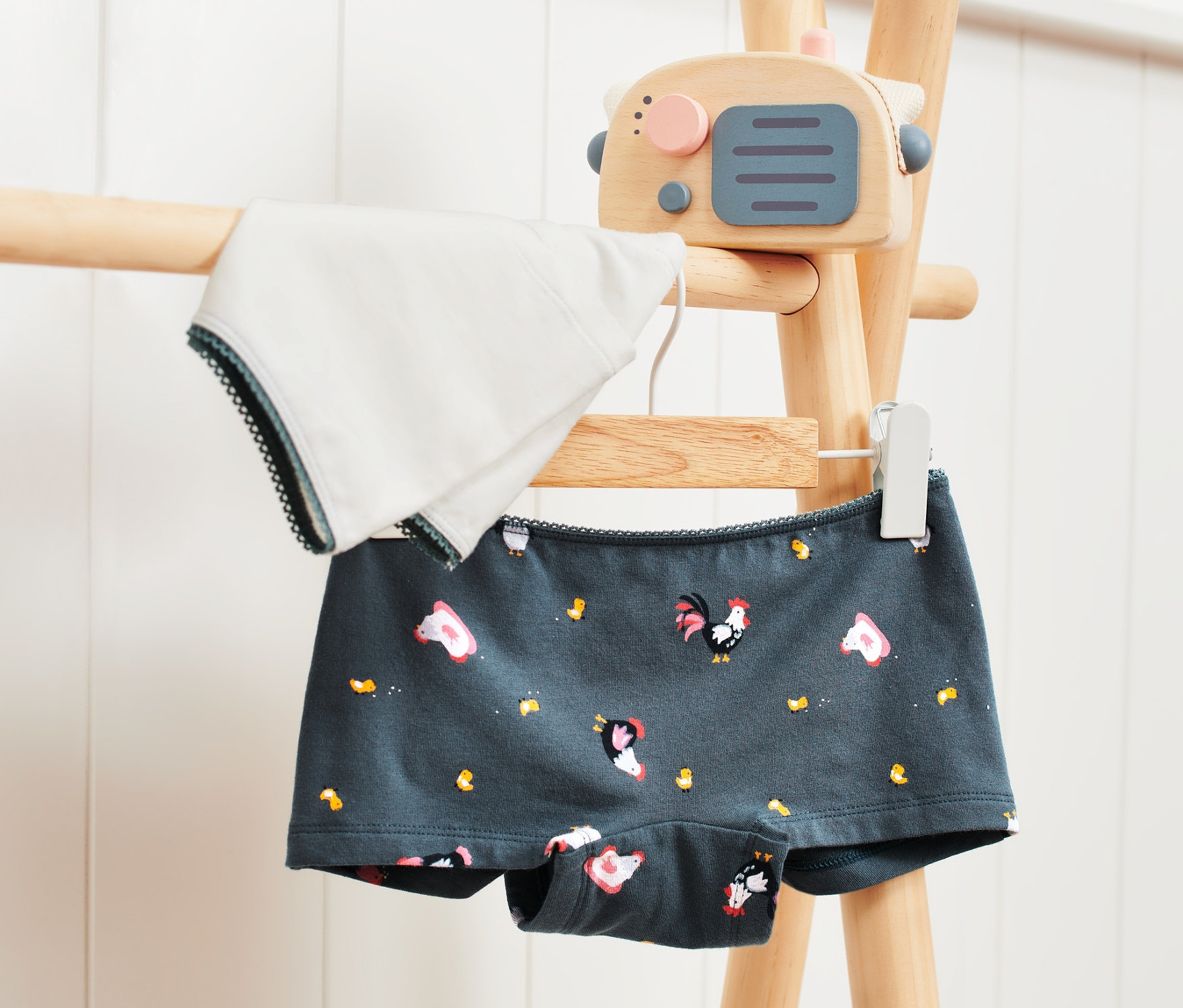 Dvoje dívčí kalhotky visí na dřevěném stojanu.