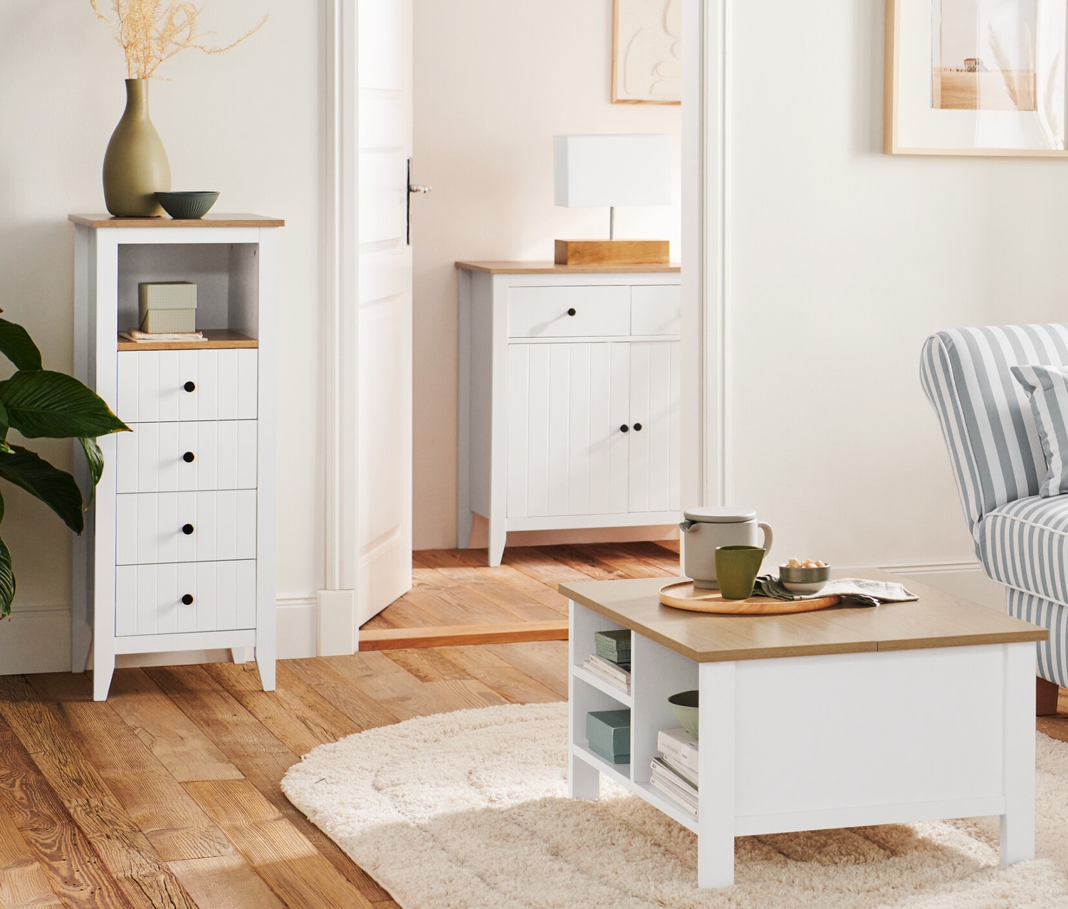 V obývacím pokoji stojí dřevěná stojací lampa Trojnožka vedle pohovky a konferenčního stolku s výklopnou funkcí. V pozadí je komoda se zásuvkami a stolní lampa s dřevěným podstavcem.