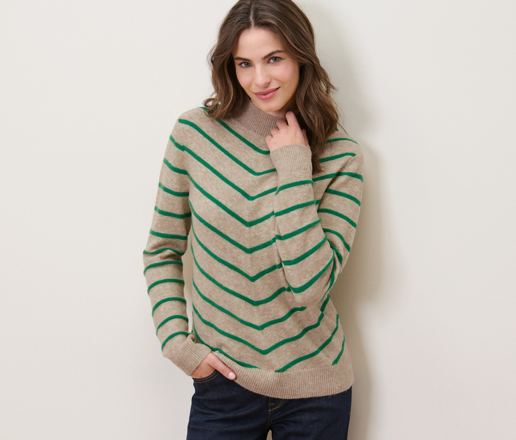 Žena pózuje na sobě krémový pletený svetr se stojáčkem a proužky.