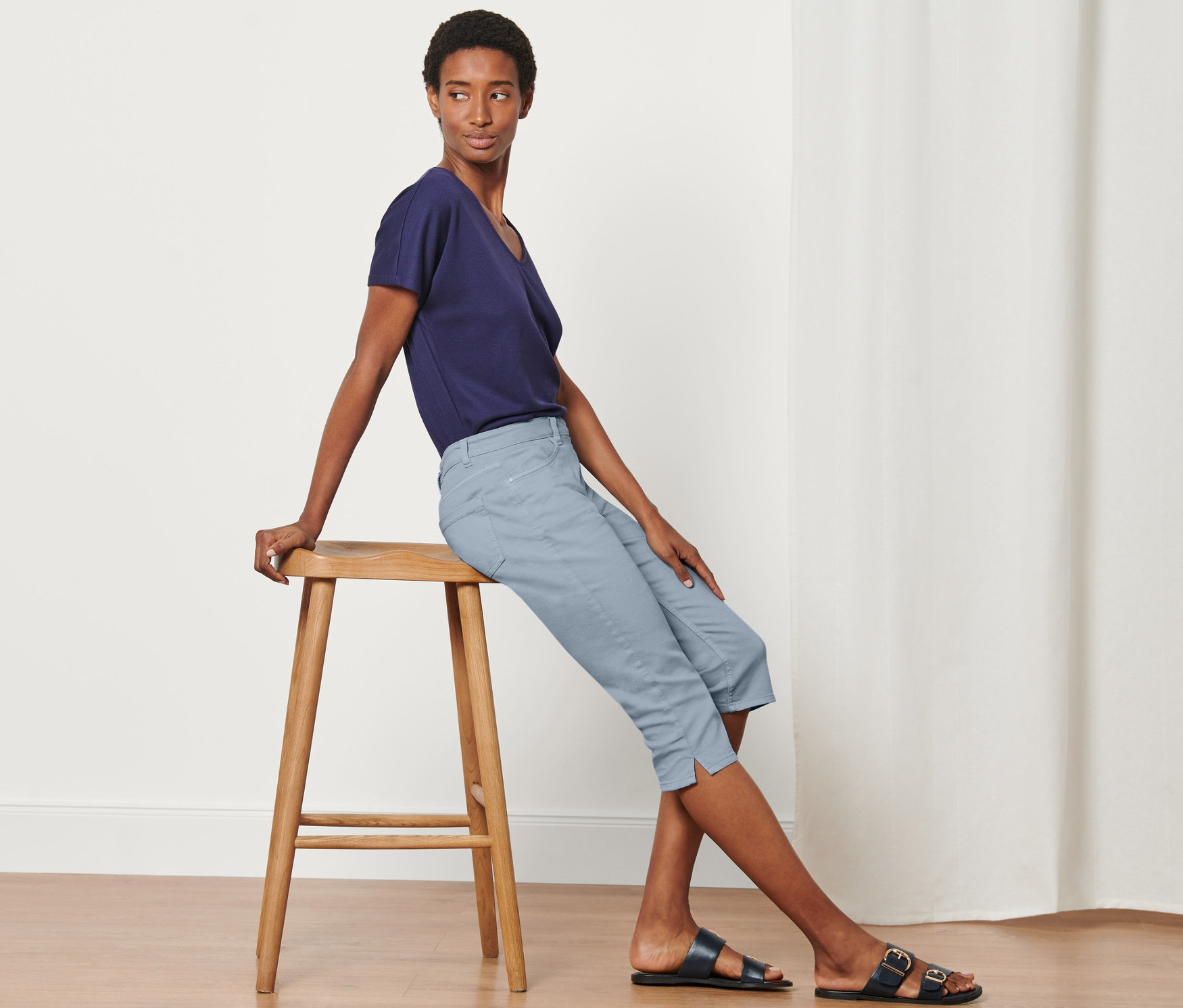 Žena sedí na stoličce a má na sobě džínové capri kalhoty.