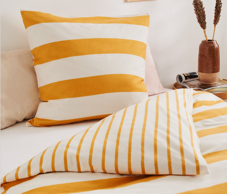 Pohled zblízka na ložní soupravu: povlak na polštář a přikrývka s žlutými a bílými pruhy. 