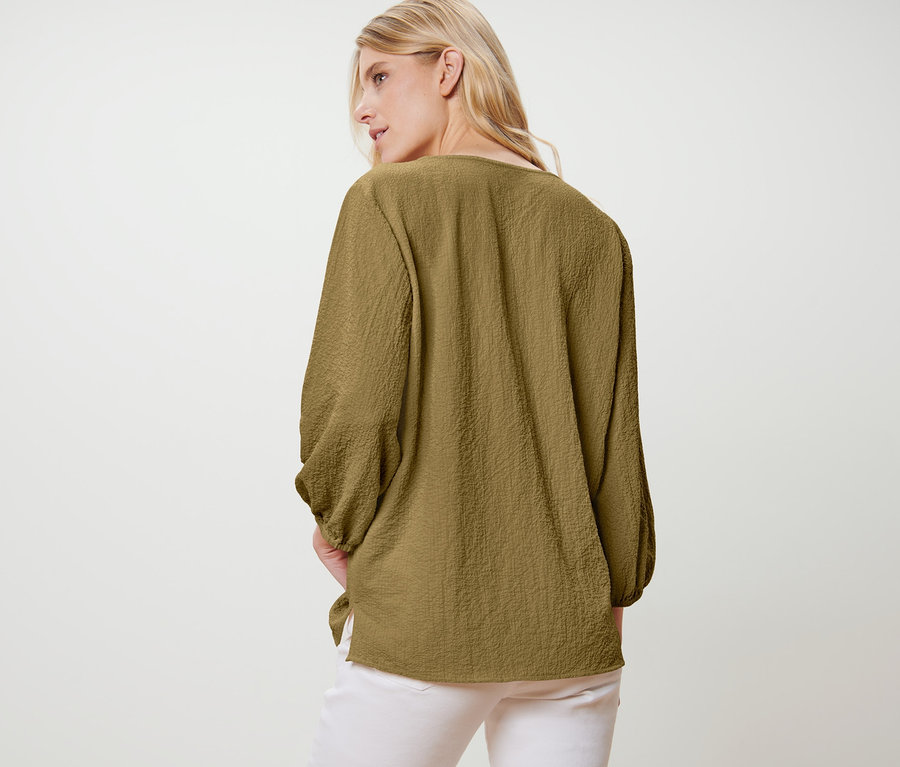 Žena v tunikové halence stojí zády k fotoaparátu.