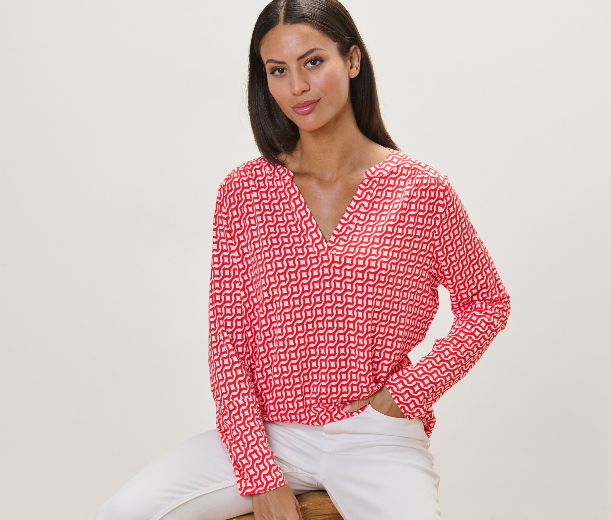 Žena sedí na stoličce a má na sobě červené halenkové triko s potiskem.