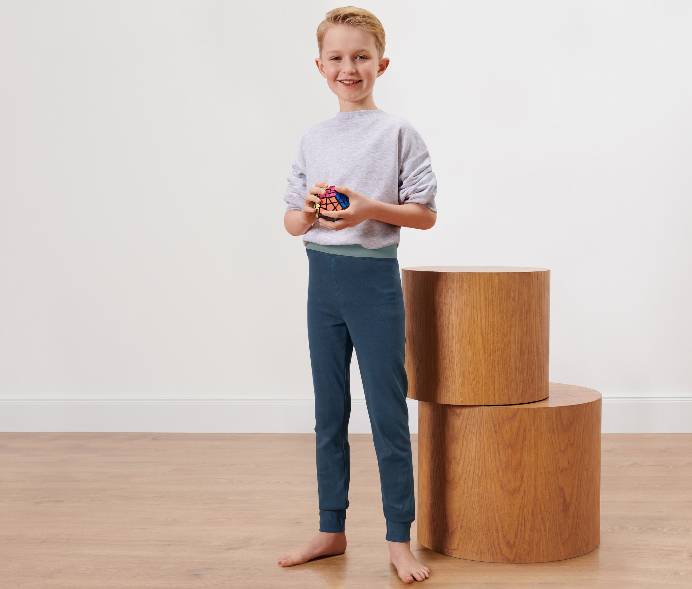Chlapec stojí a drží Rubikovu kostku. Má na sobě dlouhé dětské zimní spodky.