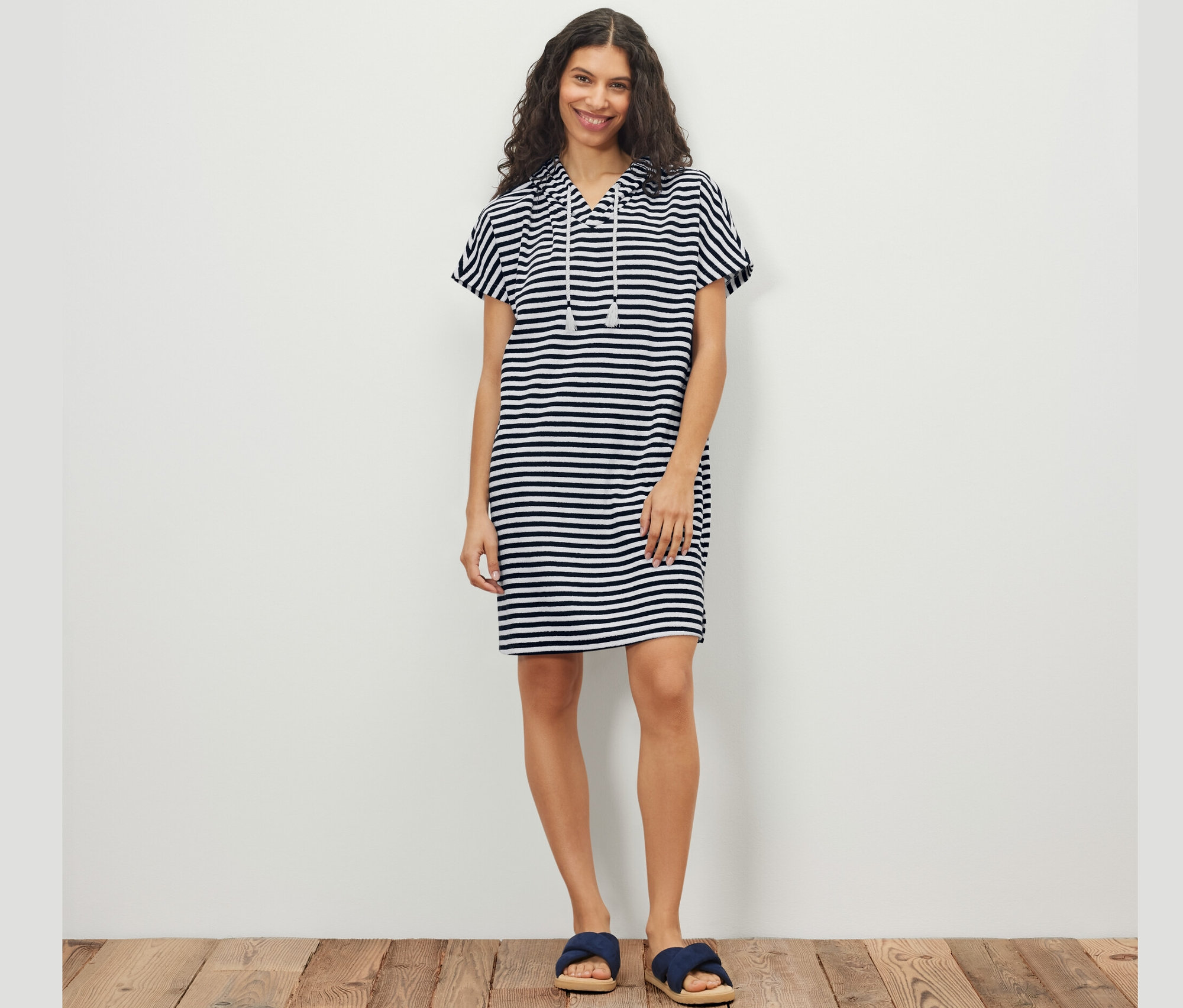 Žena pózuje v pruhovaných plážových froté šatech.
