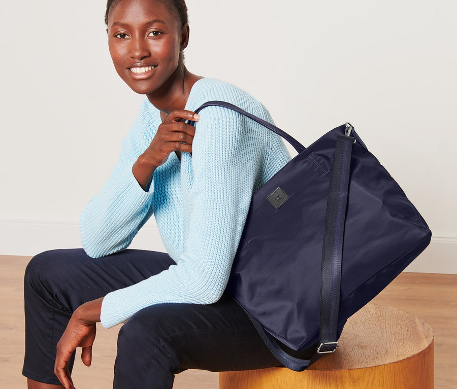 Žena sedí s nákupní taškou přes rameno.