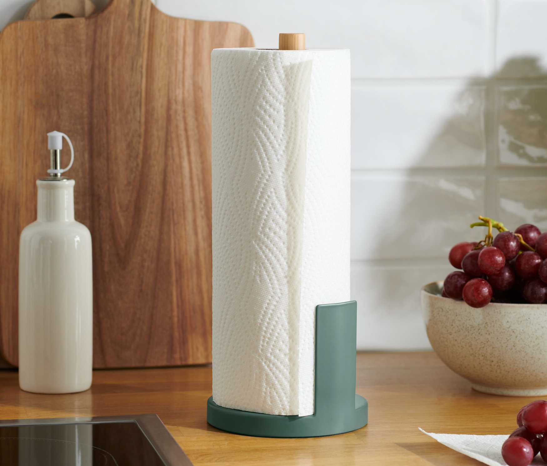 Na kuchyňské lince stojí držák na papírové utěrky vedle mísy s hrozny.