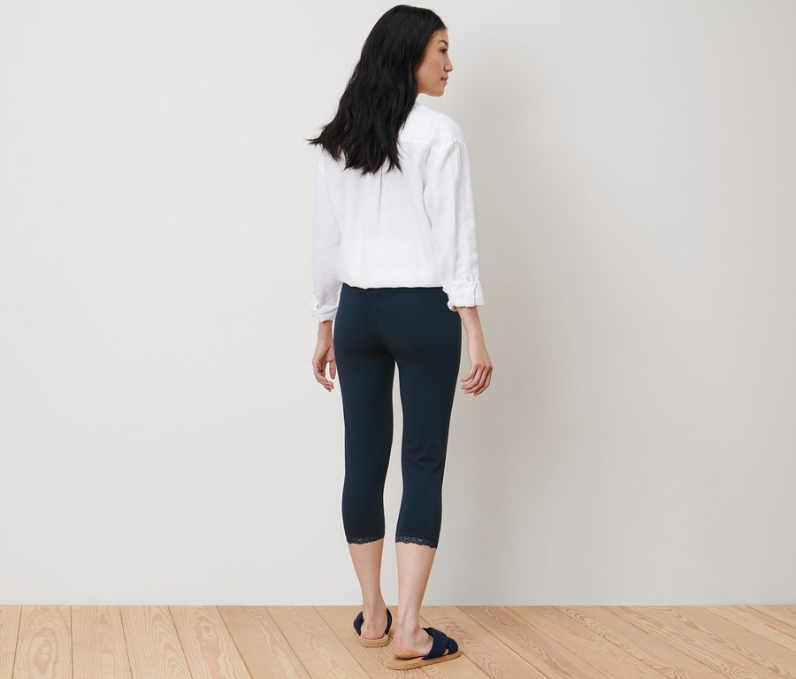 Žena stojí zády a má na sobě tmavě modré 3/4 legíny s krajkovým lemem.