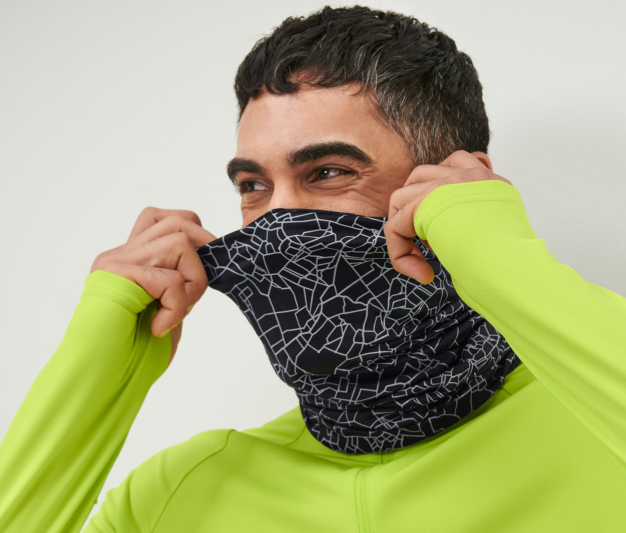 Muž si přetahuje přes obličej multifunkční černý šátek s reflexním potiskem.