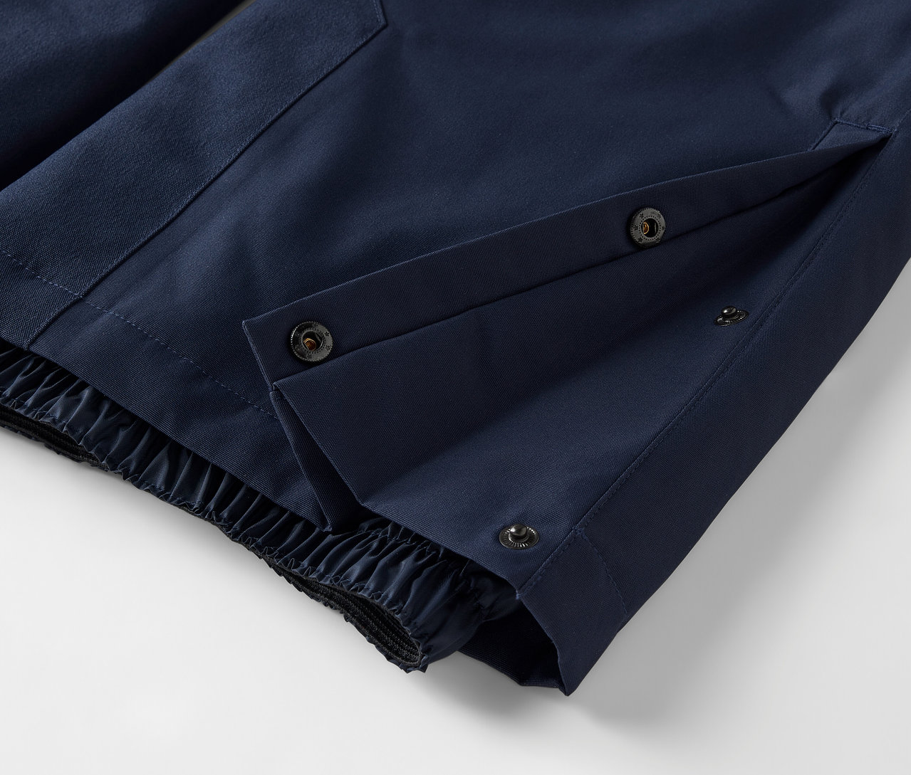 Detail modrých kalhot se zapínáním na patentky a elastickým lemem.