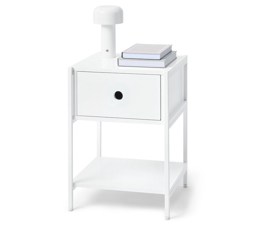 Bílý noční stolek s jednou zásuvkou, lampou a dvěma knihami nahoře.