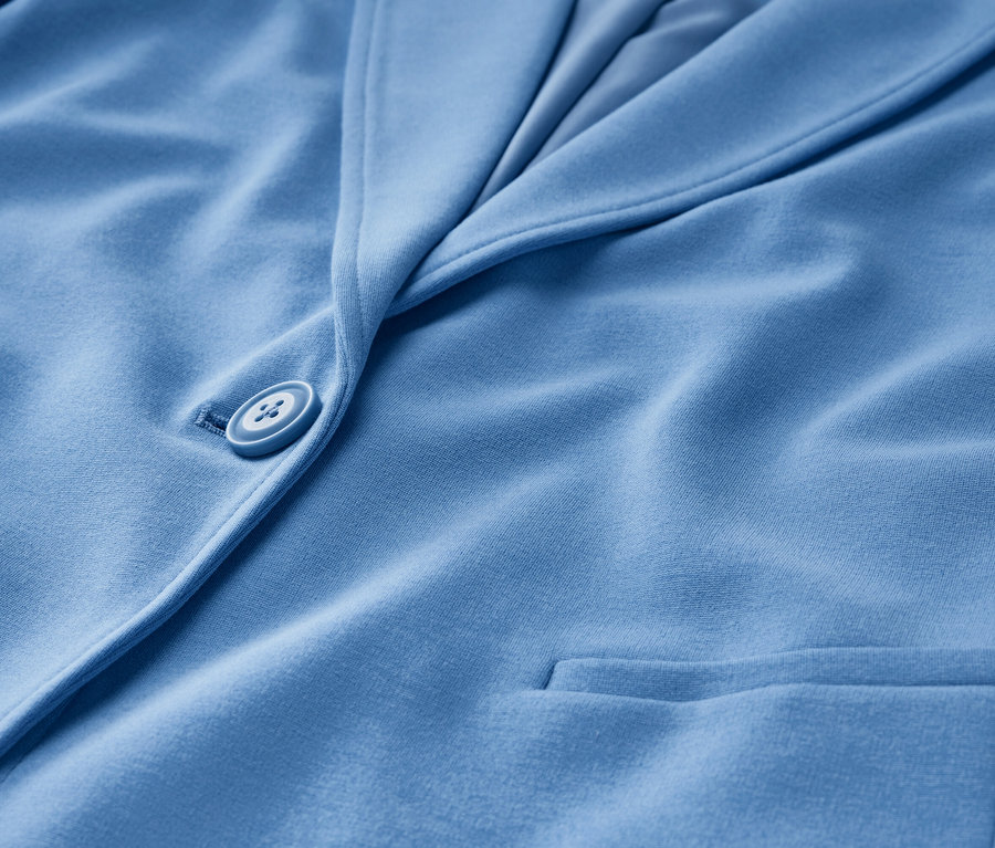 Detail světle modrého žerzejového blejzru s knoflíkem a kapsou.