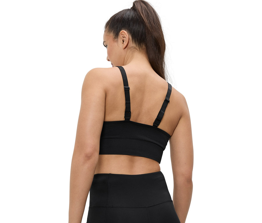 Pohled zezadu na ženu s culíkem, oblečenou do černé sportovní podprsenky a legín.