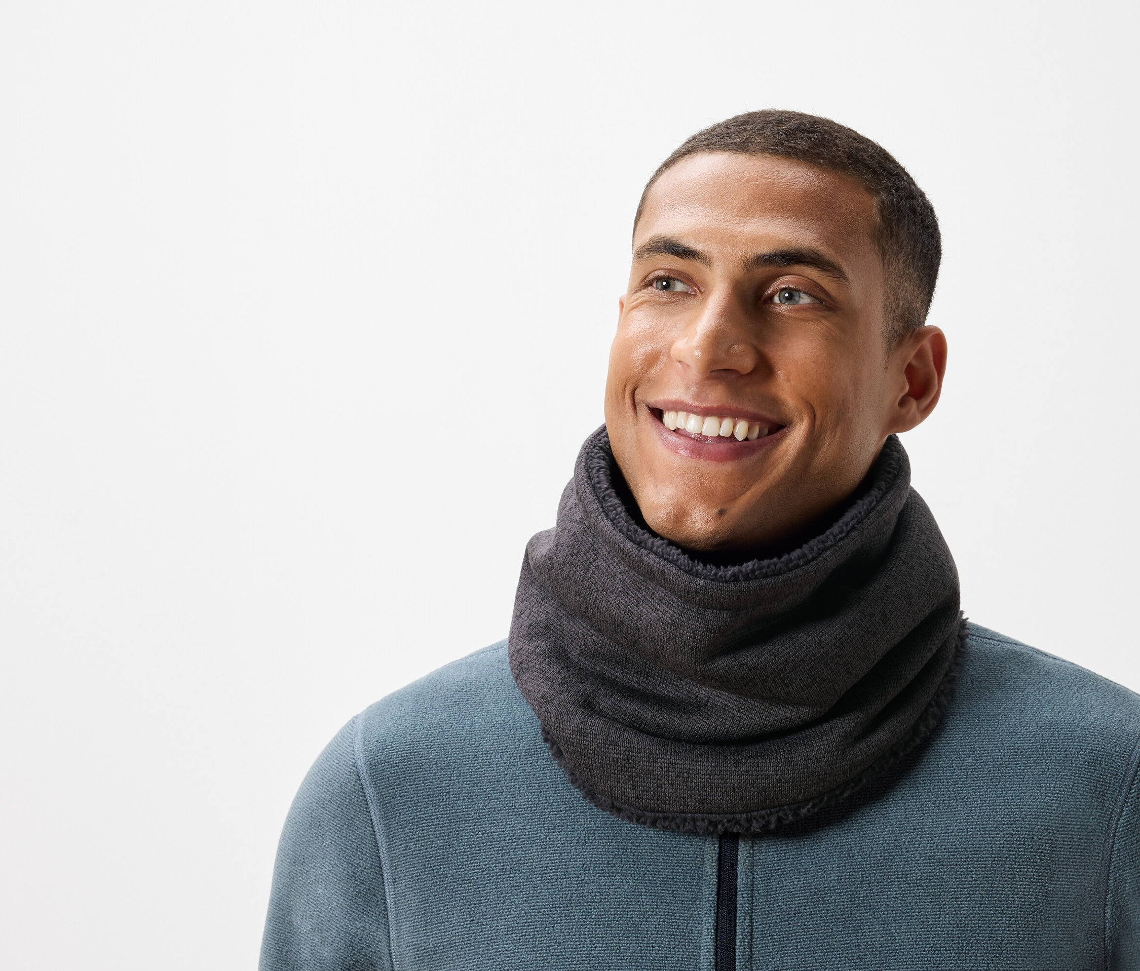 Usmívající se muž s krátkými vlasy má na sobě šedý nákrčník a modrozelený svetr.