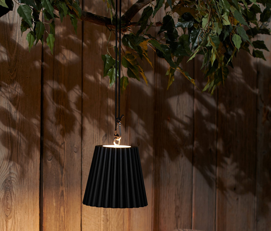 Černé akumulátorové závěsné svítidlo s LED visí nad stolem s nápoji a talíři.