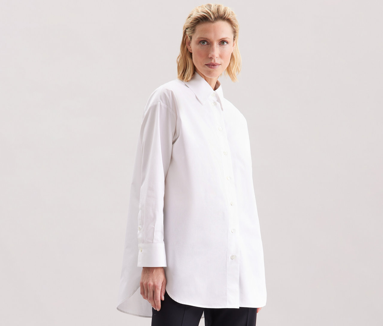 Žena má na sobě bílou dlouhou halenku oversize Seidensticker.