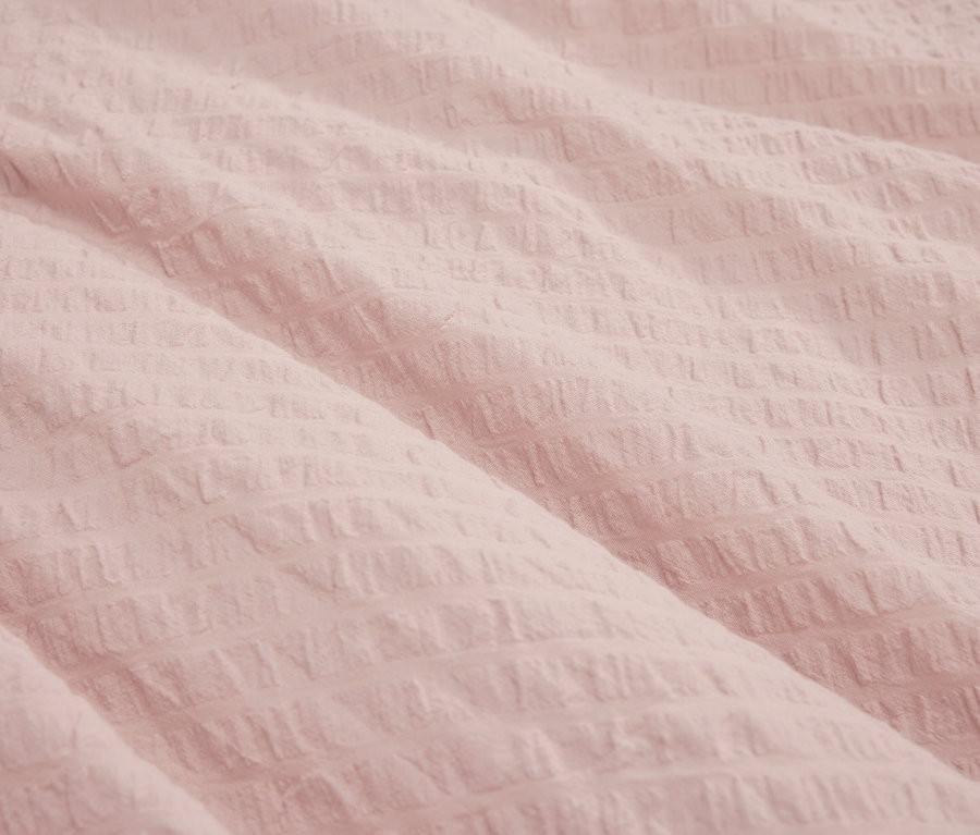 Detailní záběr na texturovanou světle růžovou látku.