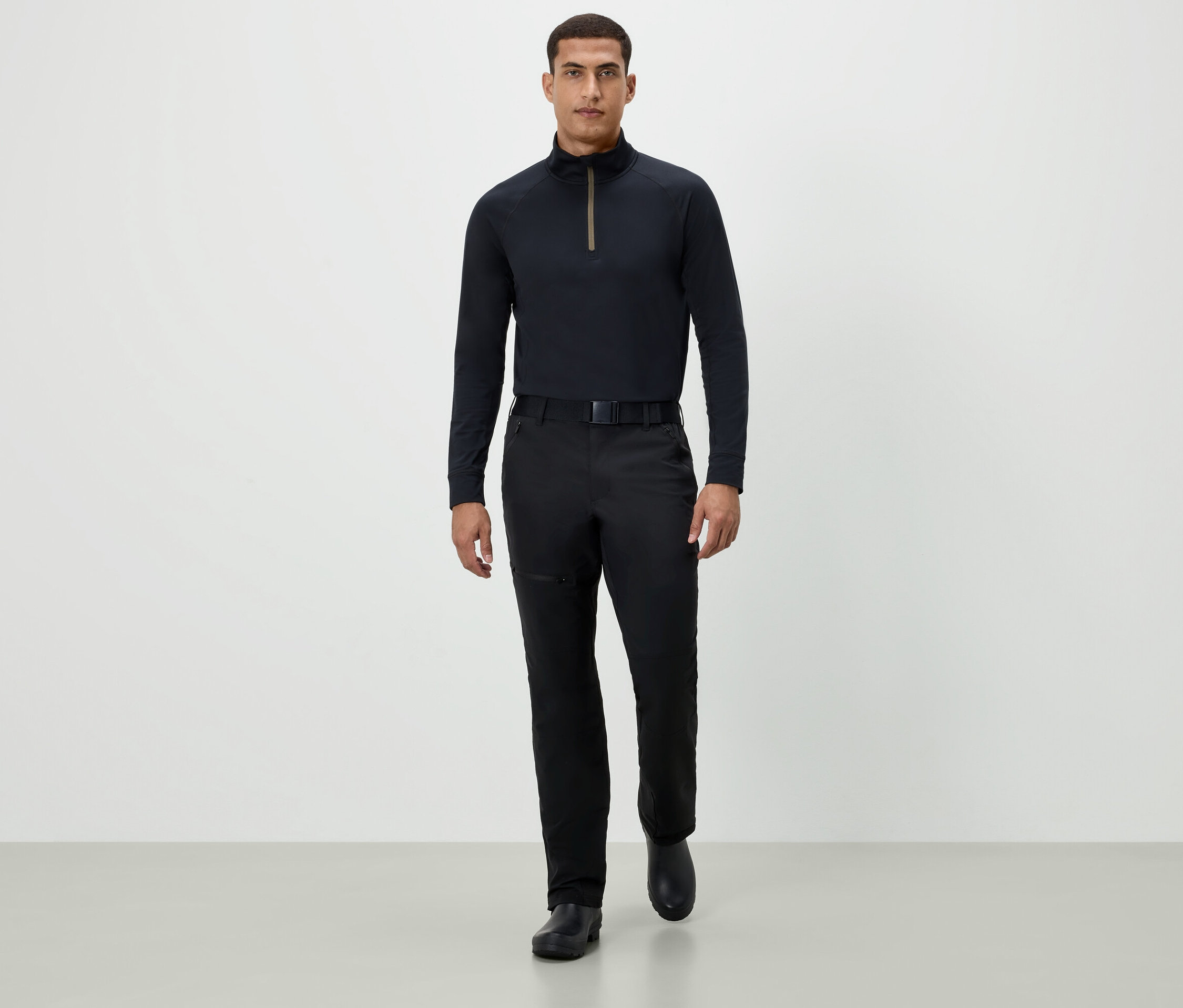 Muž kráčí vpřed v černém tričku s dlouhým rukávem, černých kalhotách a černých botách.