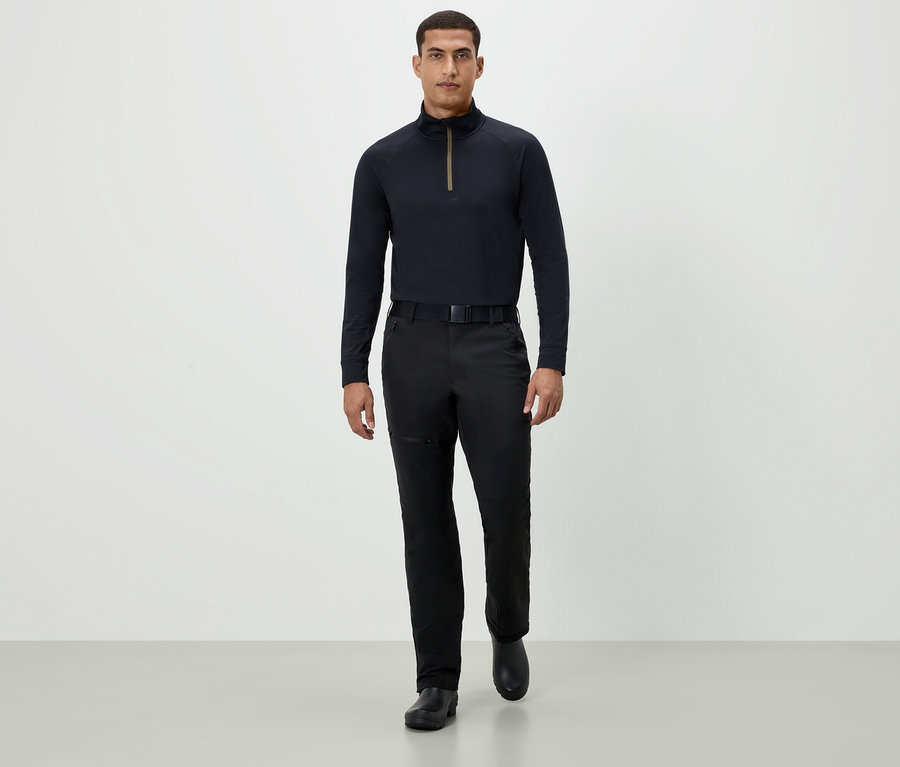 Muž kráčí vpřed v černém tričku s dlouhým rukávem, černých kalhotách a černých botách.