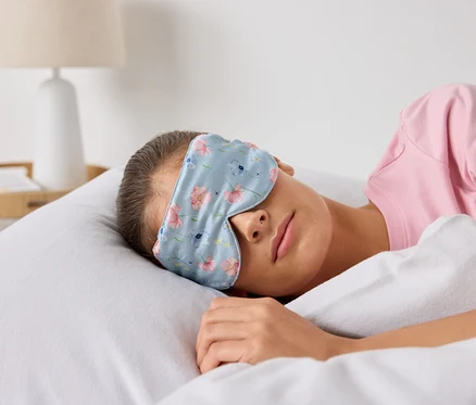 Žena spí v posteli s maskou na spaní s květinovým vzorem.
