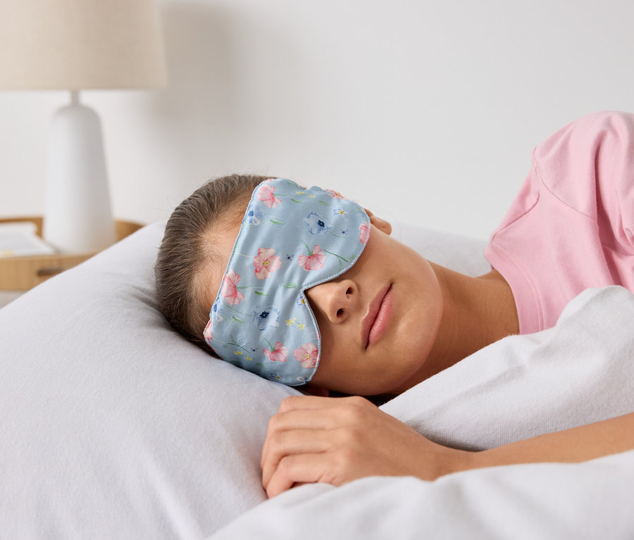 Žena spí v posteli s maskou na spaní s květinovým vzorem.