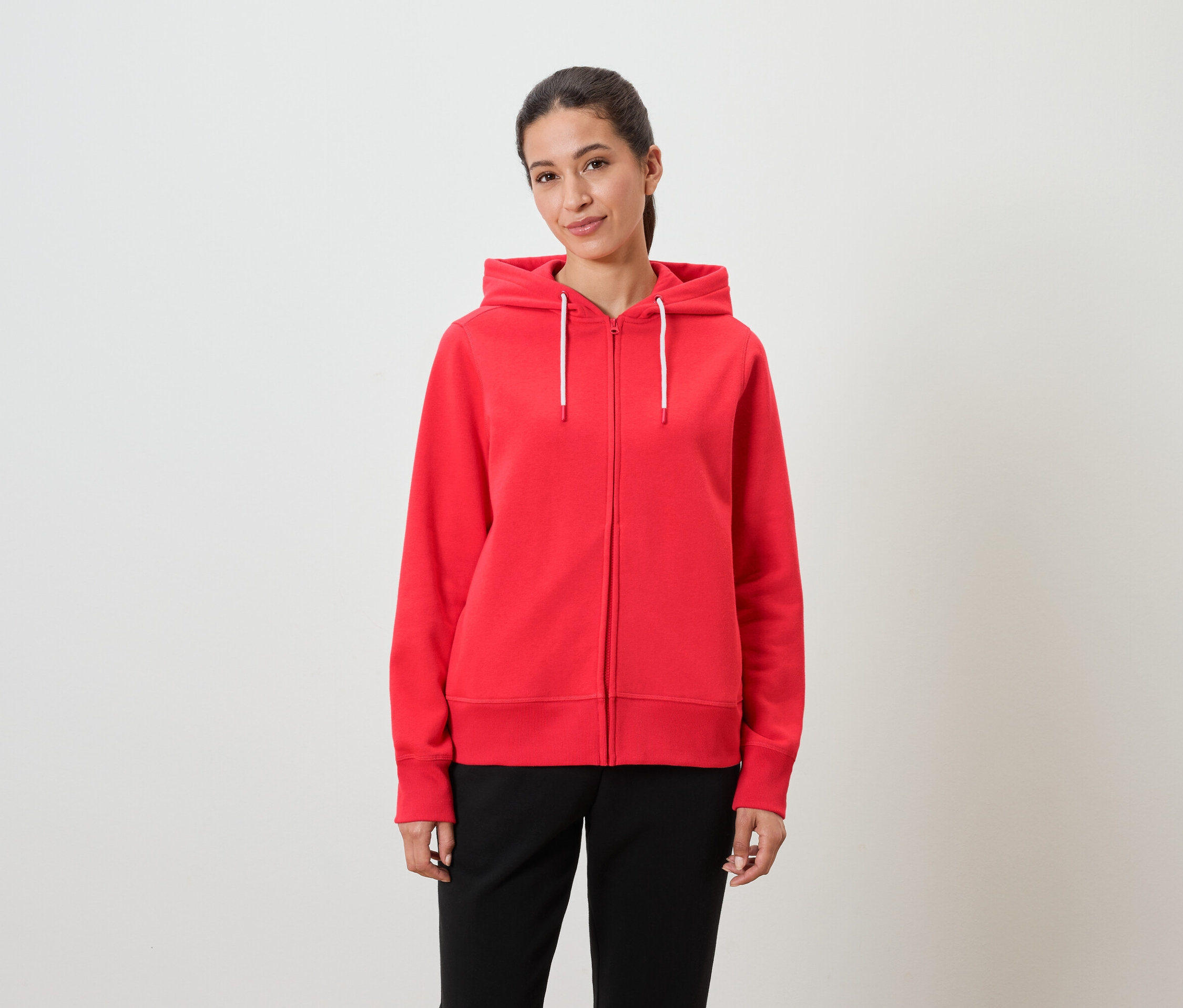 Žena má na sobě červenou mikinu s kapucí a černé kalhoty.