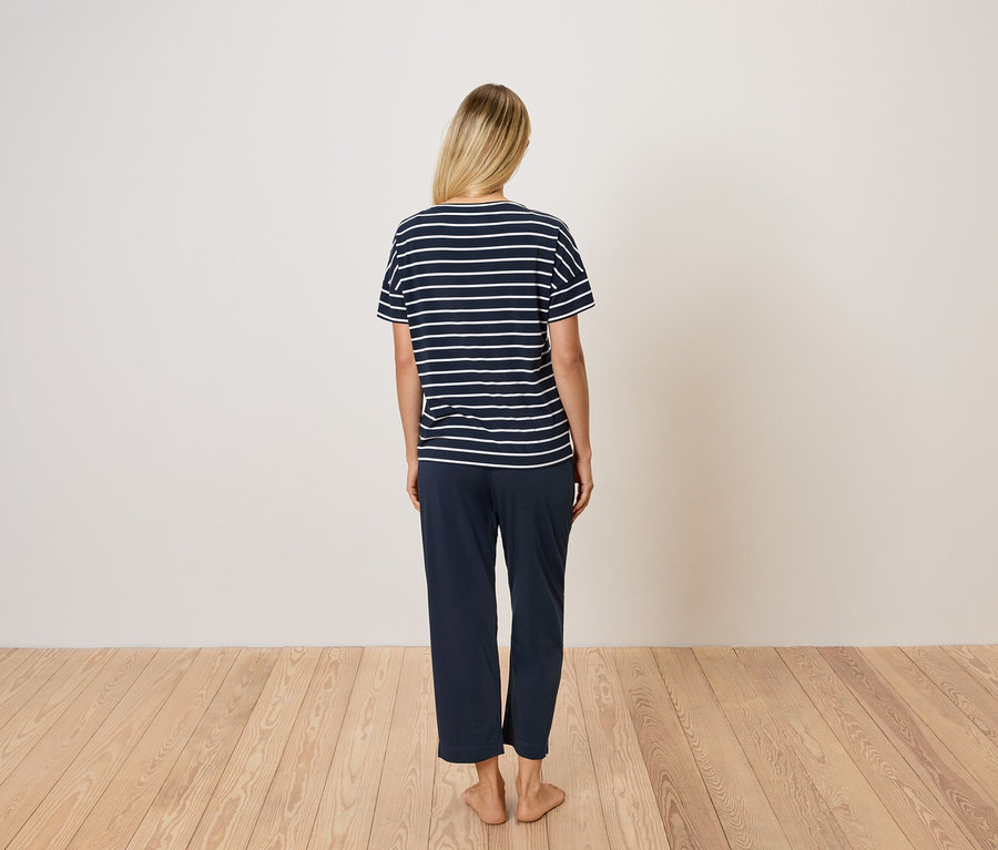 Zezadu je vidět žena s blond vlasy. Má na sobě modré pruhované tričko a modré kalhoty.