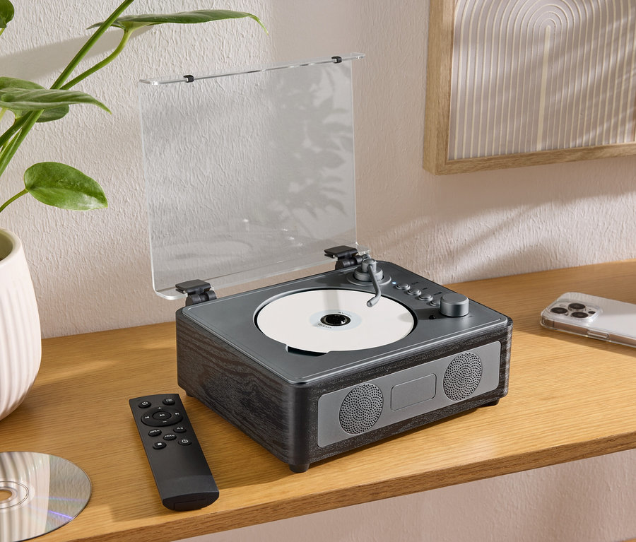 Na stole stojí reproduktor CD/Bluetooth® s CD, dálkovým ovladačem a mobilním telefonem.