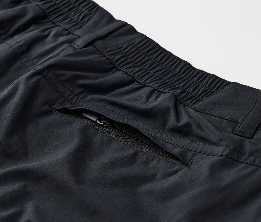 Detail černé funkční kalhoty 2 v 1 s kapsou na zip.