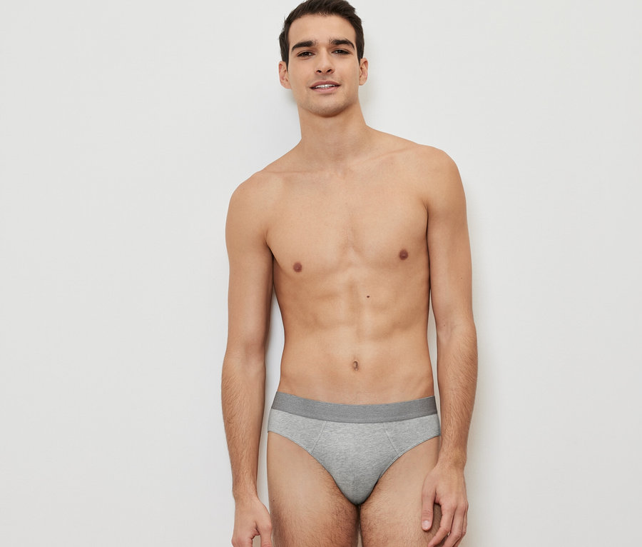 Muž pózuje na bílém pozadí a má na sobě jedny šedé slipy ze sady 4 ks.