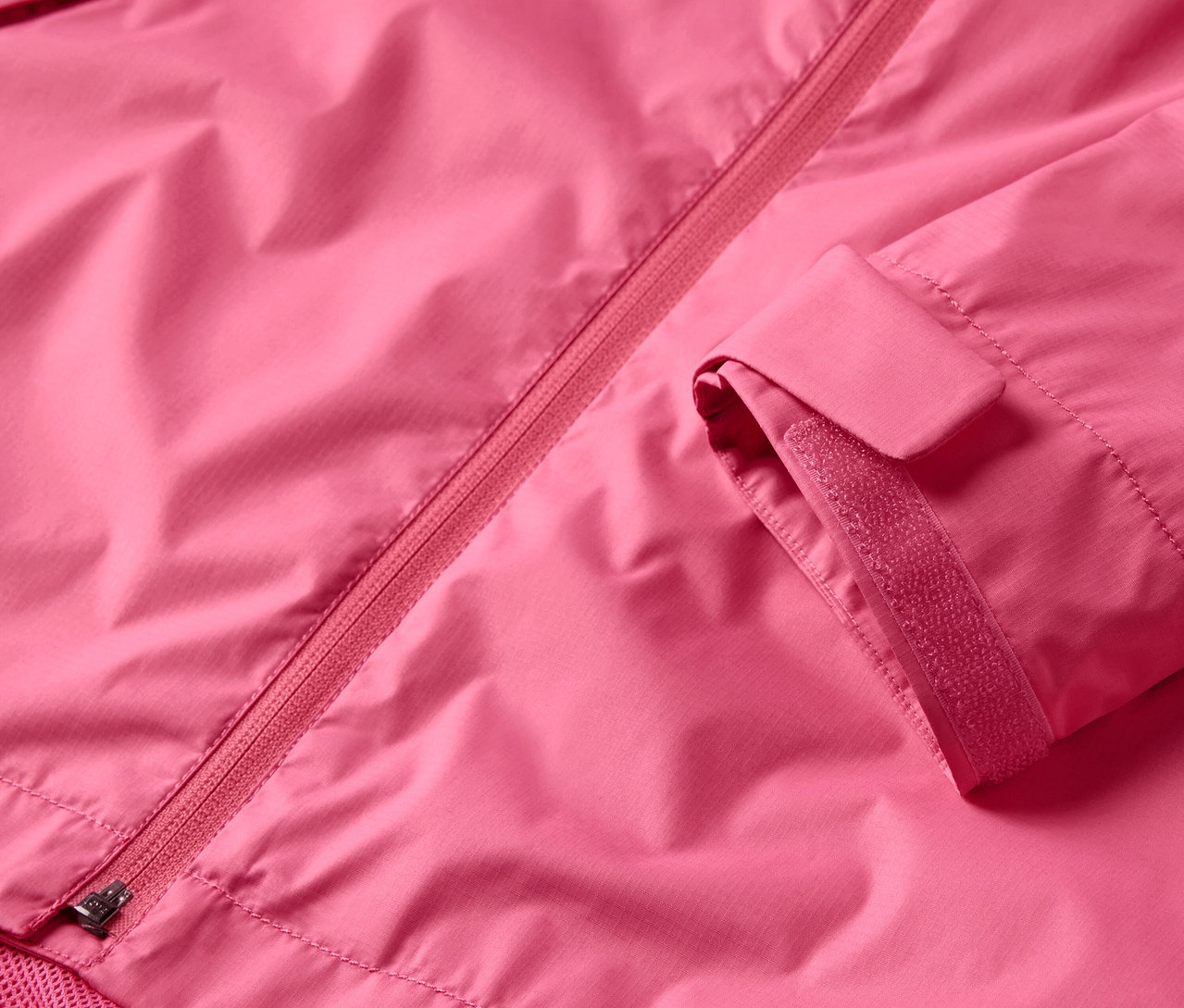 Detail růžové bundy do deště se zipem a rukávem.
