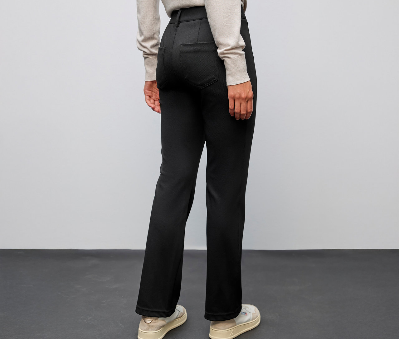 Osoba zezadu, oblečená do černých bootcut kalhot Street One a světlé obuvi.