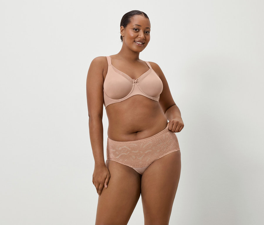 Žena s tmavou pletí má na sobě tělovou podprsenku a odpovídající krajkové kalhotky na jednoduchém pozadí.